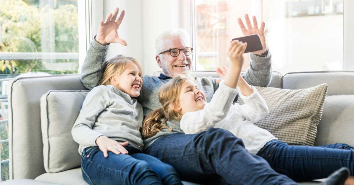 grandpére portant des les lunettes qui sourit pour le caméra de sa petite fille assis sur un canapé