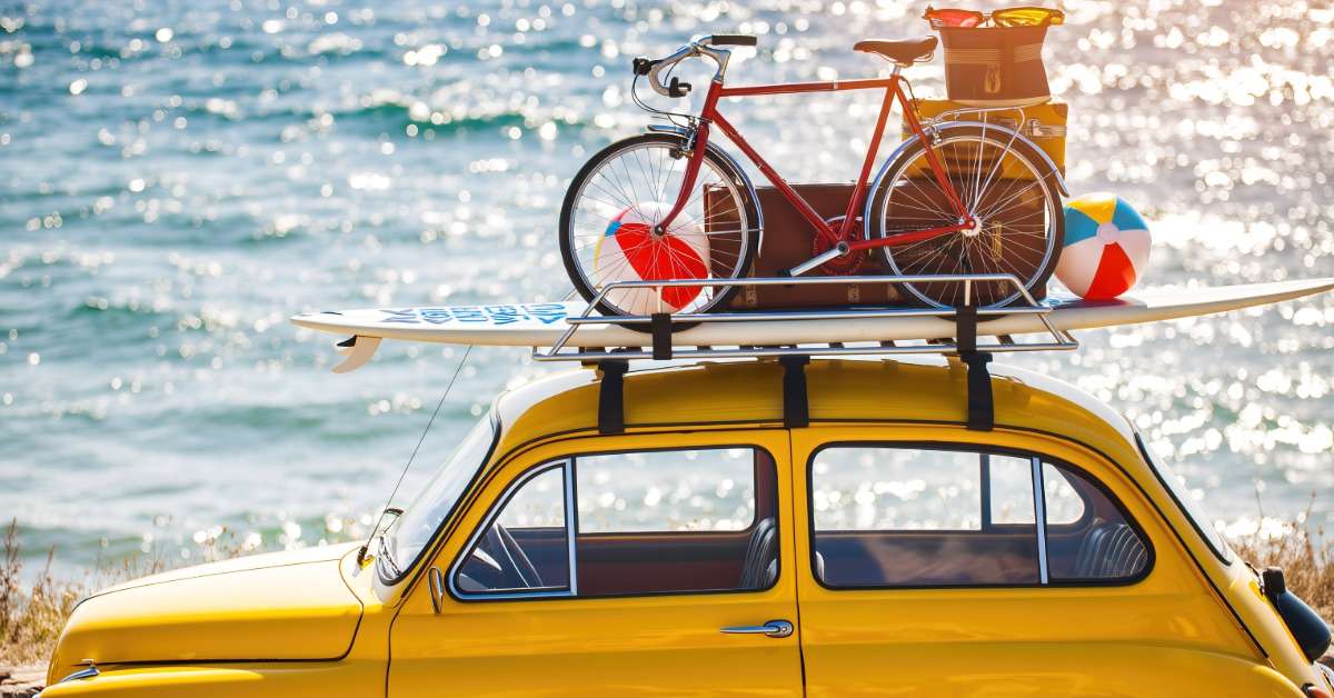 une voiture jaune  avec les bagages des vacances sur son toit en bord de mer
