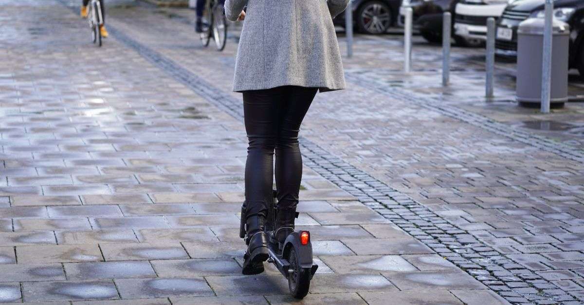 Femme à trottinette électrique roulant dans une zone piétonne