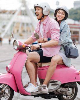 Un homme et une femme souriants à bord d’un scooter rose