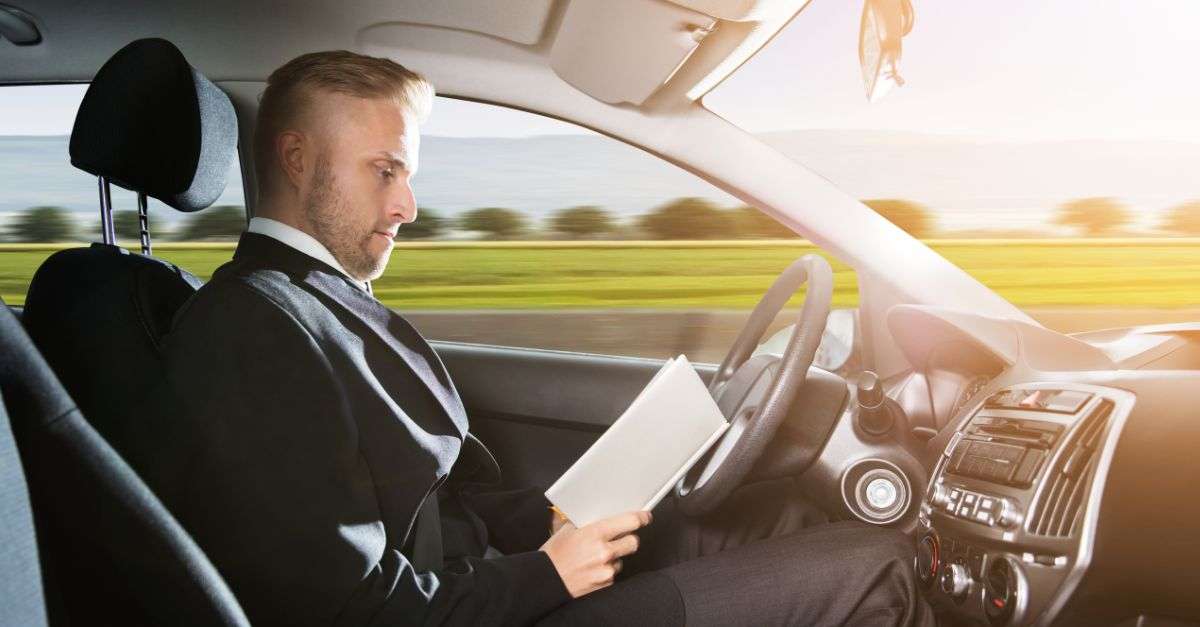 Homme en train de lire au volant d'une voiture autonome